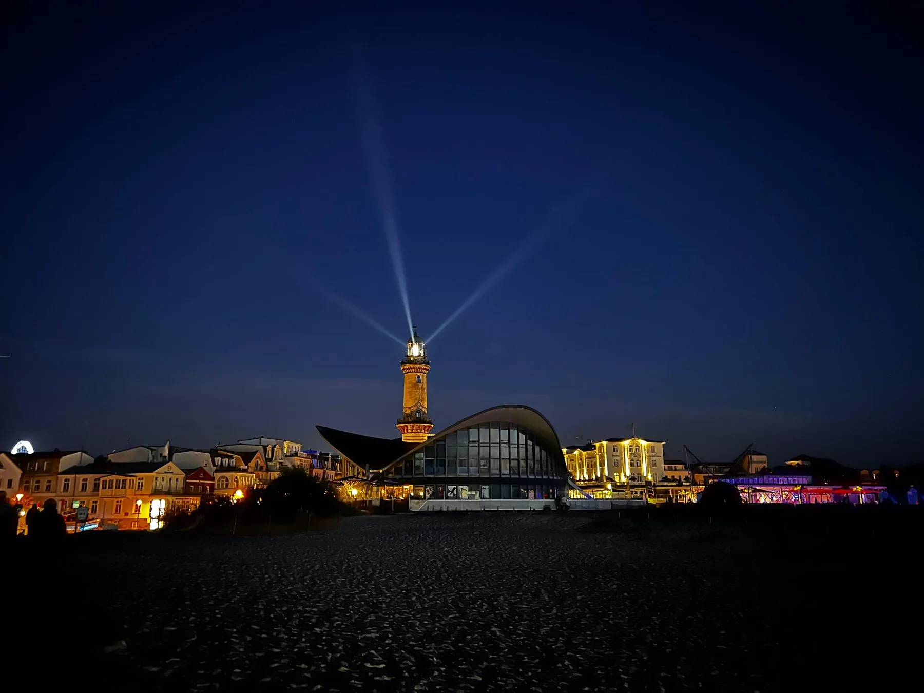 Warnemünder Leuchtturm bei Nacht mit Lichtstrahlen über Teepott und Strand